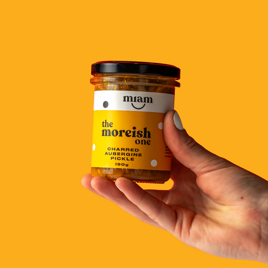 a hand holding a jar of aubergine pickle on an orange background